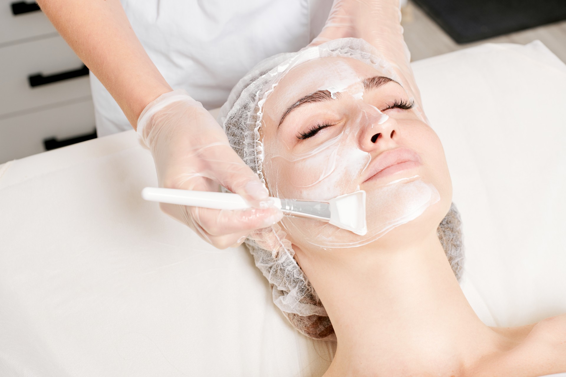 Beautician applies vitamins cream mask on woman face for rehydrate face skin in beauty salon